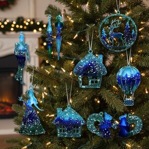 May include: A selection of blue and green glitter Christmas tree decorations. The ornaments include a mermaid, a house, a hot air balloon, a deer in a forest, and other festive shapes. The decorations are detailed with glitter and have a shimmering effect, hanging on a decorated tree.