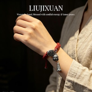 May include: Red woven bracelet with silver-colored charms. The bracelet features a circular clasp and a bell-shaped charm. The text "LIUJIXUAN" is at the top, with the words "Woven by hand, blessed with soulful energy & inner peace."