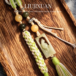 Puede incluir: Llaveros con cordones trenzados verdes y blancos, con cuentas y un colgante de gato de jade. El texto "LIUJIXUAN" es visible, junto con la frase "Woven by hand, blessed with soulful energy & inner peace."