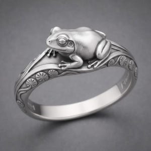 Puede incluir: Un anillo plateado con un diseño detallado de rana. La rana está posada en una hoja de nenúfar con intrincados patrones florales y de hojas. El anillo tiene un acabado pulido, mostrando la piel texturizada de la rana y los delicados detalles de la hoja de nenúfar.