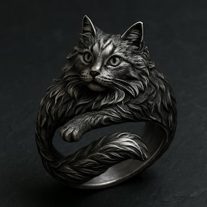 May include: A detailed silver ring featuring a sculpted cat design. The ring showcases a fluffy cat with intricate fur detailing, its paws and tail forming the band. The cat's face is centered, with attentive eyes and whiskers.