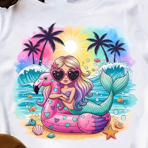 Op de afbeelding: Een wit T-shirt met korte mouwen en een kleurrijke afbeelding van een zeemeermin met lang blond haar en een hartvormige zonnebril, liggend op een roze flamingo-zwemband op het strand met palmbomen, oceaangolven en een felle zon.