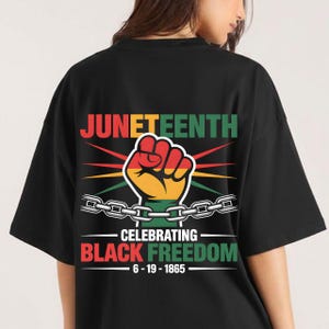 Op de afbeelding: Zwart T-shirt met een Juneteenth-afbeelding. Het ontwerp bevat het woord "JUNETEENTH" in groen en rood, een vuist en de zin "CELEBRATING BLACK FREEDOM" met de datum 6-19-1865.