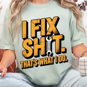 Puede incluir: Camiseta verde claro con el texto "I FIX SHIT. THAT'S WHAT I DO." en amarillo y negro. Una llave inglesa blanca está centrada entre las palabras. Una prenda de vestir informal.