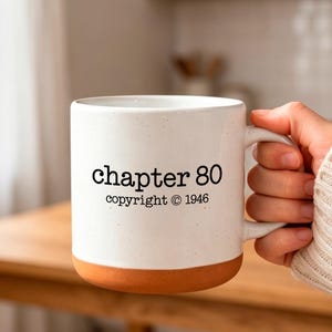 Op de afbeelding: Een witte keramische mok met een gespikkelde afwerking en een terracotta-kleurige basis. De voorzijde van de mok is voorzien van zwarte tekst met "chapter 80" op de bovenste regel en "copyright © 1946" op de onderste regel in een strak lettertype.