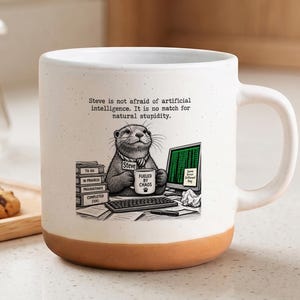 May include: A white ceramic mug with a speckled finish and a terracotta-coloured base. The front features an illustration of an otter at a desk with a computer, a stack of books, and the text: "Steve is not afraid of artificial intelligence. It is no match for natural stupidity."