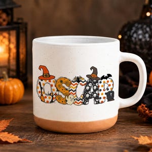 May include: A white ceramic mug with a speckled finish and a terracotta-colored base. The front features the name OSCAR in large, patterned letters decorated with Halloween motifs including witch hats, a broom, a ghost, and a tombstone.