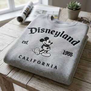 Op de afbeelding: Een set van drie keramische mokken met een gespikkelde, cr&egrave;mekleurige glazuur. Elke mok heeft een ander handgeschilderd bloemmotief in blauw, groen en geel. De mokken hebben een eenvoudige, moderne vorm.