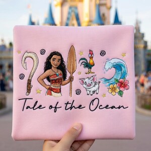 Pu&ograve; includere: Un tessuto quadrato rosa con un disegno ricamato raffigurante una donna, un gancio, una pagaia di legno, un gallo, un maiale, un'onda e fiori. Il testo "Tale of the Ocean" &egrave; scritto sotto.