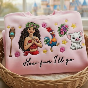 Może przedstawiać: Jasnor&oacute;żowa bluza z haftowanymi postaciami i napisem "How far I'll go". Projekt zawiera kobietę, koguta, świnię oraz elementy kwiatowe i gwiazdki. Bluza jest złożona w wiklinowym koszu.