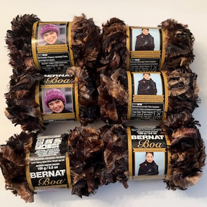 May include: Five skeins of Bernat Boa yarn in a dark brown and black variegated colorway. Each skein features a paper label with a photograph of a person wearing a finished garment, product weight of 100 grams, and free pattern information.