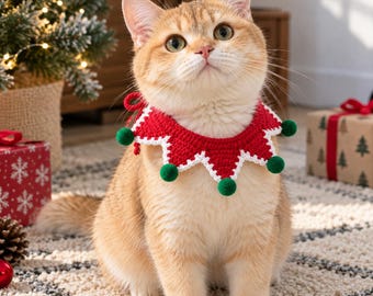 May include: A ginger cat wearing a red and white crocheted collar with a pointed, star-like edge. The collar features small green pom-poms attached to each of the points and is tied at the back with a red yarn string around the cat's neck.