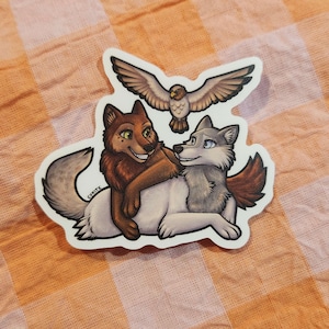 May include: A sticker featuring a brown wolf embracing a gray wolf, with a brown and white owl above them. The sticker has a white border and the artist's name, "CYKITE", is visible.