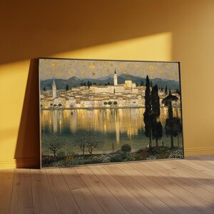 May include: A rectangular framed wall art print depicting a lakeside town at twilight. The scene features golden reflections on the water, a dense cluster of buildings with a tall tower, dark cypress trees in the foreground, and a starry sky.