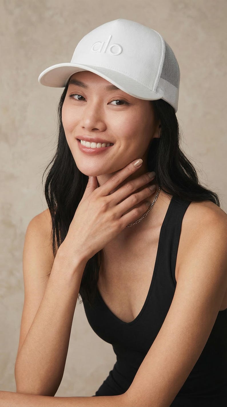 Puede incluir: Gorra de b&eacute;isbol blanca con la parte trasera de malla y la palabra "alo" bordada en la parte delantera. La gorra la lleva una persona que lleva una camiseta sin mangas negra.