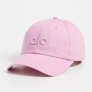 Puede incluir: Gorra de b&eacute;isbol rosa claro con la palabra "alo" bordada en la parte delantera. La gorra tiene una visera curva y un peque&ntilde;o bot&oacute;n en la parte superior. Este accesorio casual es elegante.