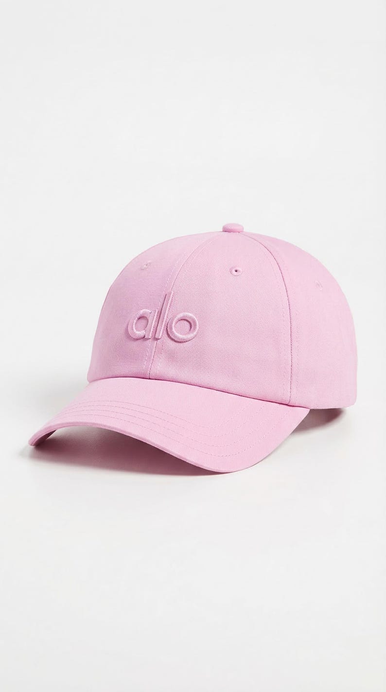 Puede incluir: Gorra de b&eacute;isbol rosa claro con la palabra "alo" bordada en la parte delantera. La gorra tiene una visera curva y un peque&ntilde;o bot&oacute;n en la parte superior. Este accesorio casual es elegante.