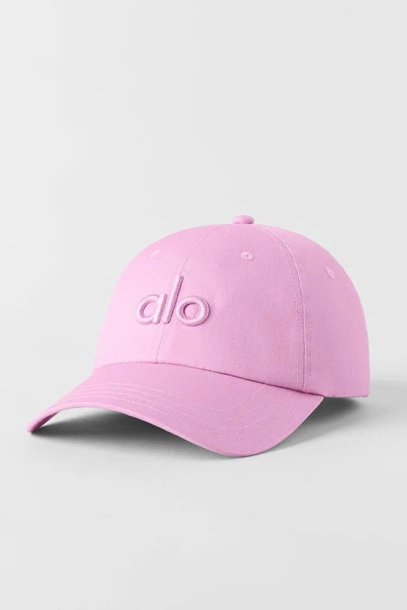 Puede incluir: Gorra de b&eacute;isbol rosa claro con visera curva. La gorra presenta las letras "alo" bordadas en la parte delantera. El sombrero est&aacute; hecho de una tela suave y tiene una corona redondeada.