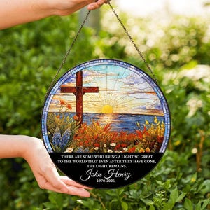 May include: A round stained glass window with a cross, sunset, and floral design. The text reads "THERE ARE SOME WHO BRING A LIGHT SO GREAT TO THE WORLD THAT EVEN AFTER THEY HAVE GONE, THE LIGHT REMAINS. John Henry 1970-2026."