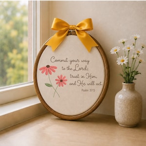 Peut inclure: Un tambour à broder circulaire en bois contenant un tissu blanc cassé avec des fleurs roses brodées et le texte : Commit your way to the Lord; trust in Him, and He will act. Psalm 37:5. Un nœud en satin jaune moutarde est fixé au sommet.