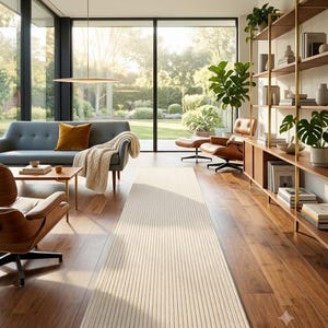 Peut inclure: Un long tapis rectangulaire de couleur beige clair avec une texture subtile à rayures verticales. Le tapis est placé au centre sur un plancher en bois poli, s'étendant du premier plan vers le milieu de l'espace de vie.