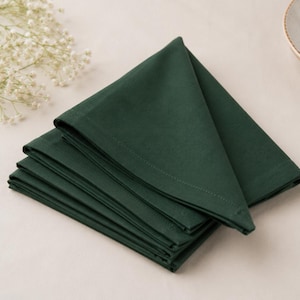 Peut inclure: Une pile de quatre serviettes en tissu vert forêt foncé pliées. Chaque serviette est de forme carrée avec des bords cousus nets, disposées en une formation triangulaire soignée et superposée pour montrer la couleur verte unie.