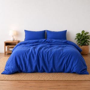 May include: A vibrant royal blue duvet cover set featuring a textured fabric finish. The bedding ensemble includes a large duvet cover draped over a bed and two matching rectangular pillow shams positioned upright against the head of the bed.