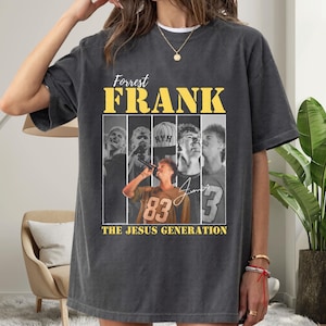 May include: Dark gray t-shirt featuring a graphic of Forrest Frank with the text "Forrest Frank" in yellow block letters. The shirt includes images of Frank and the text "The Jesus Generation".