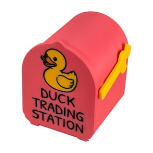 May include: A pink mailbox-shaped container with a yellow duck illustration and the text "DUCK TRADING STATION." The mailbox has a yellow handle and is designed to resemble a traditional mailbox.
