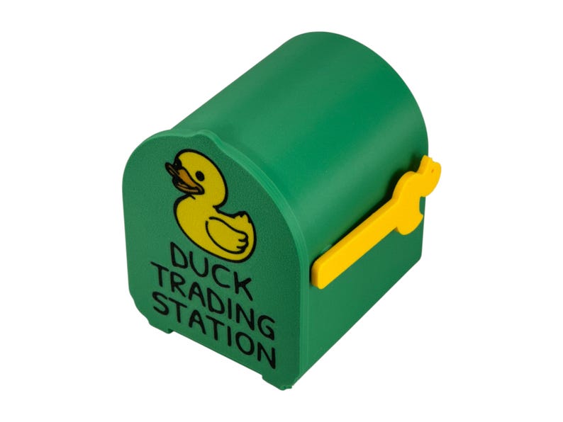 May include: A green, duck-shaped mailbox with a yellow duck graphic and the words "Duck Trading Station." The mailbox has a yellow handle. The design is whimsical and playful.
