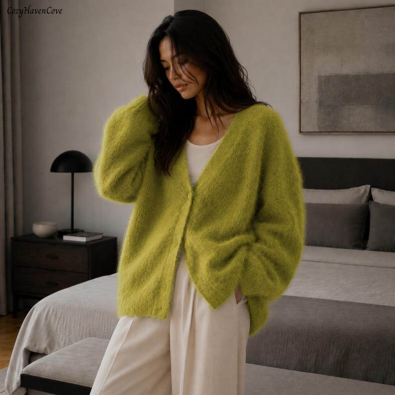 May include: A fuzzy, lime green V-neck cardigan with long sleeves and a single button closure, worn over a plain white tank top and light-colored trousers. The knit fabric has a soft, textured appearance with a visible, slightly loose weave.