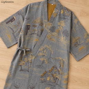 May include: Gray kimono robe with a landscape design in gold and brown. The robe features a tie closure and wide sleeves. The fabric has a textured appearance, and the design includes trees, buildings, and a serene landscape.