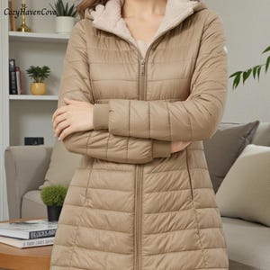 Può includere: Cappotto trapuntato beige con cappuccio e cerniera a tutta lunghezza. Il cappotto ha una morbida fodera colorata chiara nel cappuccio e un piccolo logo sulla parte superiore del braccio. Le maniche hanno polsini a coste. Progettato per calore e protezione.