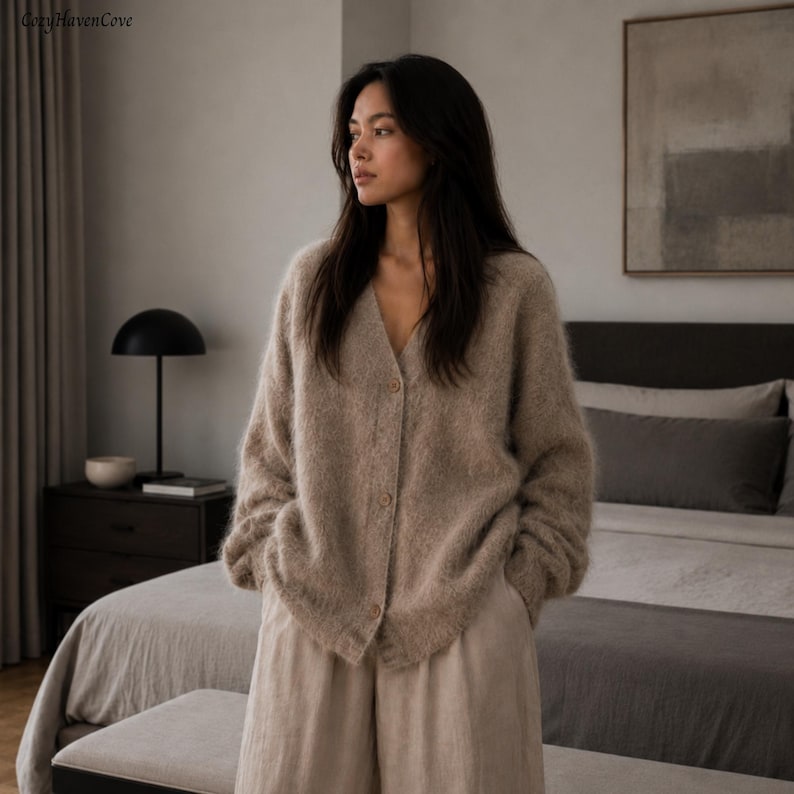 May include: A beige V-neck cardigan with a fuzzy, textured knit finish and long sleeves. The garment features a front button closure with three visible buttons and a relaxed, loose fit. The material has a soft, brushed appearance throughout.