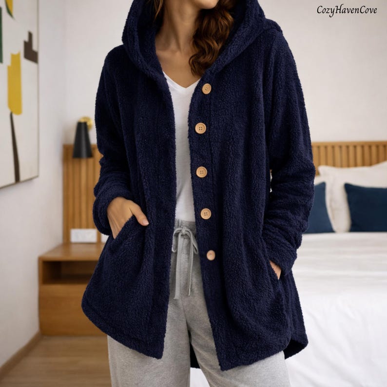 May include: A navy blue hooded jacket with wooden buttons and two front pockets. The jacket is made of a soft, plush material. The text "CozyHavenCove" is in the upper right corner. This cozy jacket is perfect for lounging.