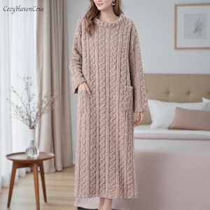 Può includere: Lungo abito in maglia a trecce marrone chiaro con maniche lunghe e due tasche anteriori. L'abito ha uno scollo tondo e un aspetto morbido e strutturato. Il marchio "CozyHavenCove" è visibile in alto a sinistra.