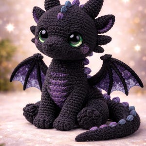 Puede incluir: Un dragón negro hecho a mano con ganchillo y detalles morados. El dragón tiene grandes ojos verdes, pequeños cuernos y alas con la parte inferior morada. Está sentado, con la cola enroscada y las alas ligeramente extendidas. El fondo es borroso.