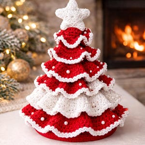 Puede incluir: Adorno de árbol de Navidad hecho a mano. El árbol está tejido a ganchillo con hilo rojo y blanco, con una estrella en la parte superior y detalles de perlas. El árbol mide aproximadamente 18 cm de alto, ideal para decoraciones navideñas.