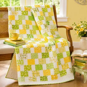 May include: A patchwork quilt featuring a repeating grid of white, bright yellow, and lime green fabric squares with various floral and geometric patterns. The quilt is draped over a wooden chair, showcasing a quilted texture and stitched borders.
