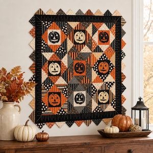 Peut inclure: Une courtepointe murale carrée présentant une grille de neuf blocs de citrouilles d'Halloween, entourée d'une bordure noire et d'un bord en dents de scie. Les tissus présentent des motifs orange, noirs et crème à rayures, pois et citrouilles.