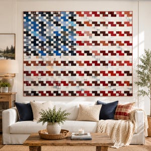 Puede incluir: Una gran colcha de pared rectangular con un diseño de patchwork que imita la bandera estadounidense. La colcha está compuesta por pequeños cuadrados en tonos azules, blancos y rojos, dispuestos en una cuadrícula que crea un aspecto tejido.