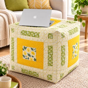 May include: A square fabric ottoman featuring a patchwork design with yellow and green floral patterns, white fabric with a subtle yellow grid, and solid yellow polka dot sections. A silver laptop is placed on the top surface of the ottoman.