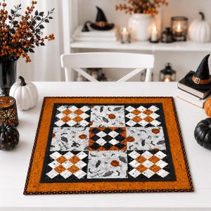 Puede incluir: Un camino de mesa cuadrado acolchado con un diseño de patchwork que alterna bloques de tela a cuadros naranja y blanca con tela blanca estampada con murciélagos negros, arañas y calabazas naranjas, todo enmarcado por un borde naranja sólido.