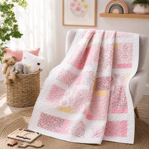 Puede incluir: Una colcha de retazos con un patrón repetitivo de cuadrados de tela blanca intercalados con cuadrados de estampado floral en tonos rosa, amarillo y lavanda suave. La colcha presenta una textura acolchada con costuras detalladas.