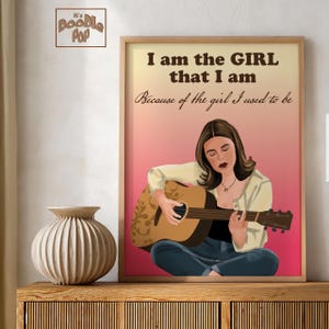 May include: A framed wall art print featuring an illustration of a person with brown hair playing an acoustic guitar. The text reads: I am the GIRL that I am Because of the girl I used to be. The background is a gradient of peach to pink.