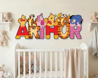 May include: A colorful wall decoration spelling "ARTHUR" with characters from Winnie the Pooh. The letters are red, orange, and pink, with the characters positioned above. The scene includes a white crib and stuffed animals.