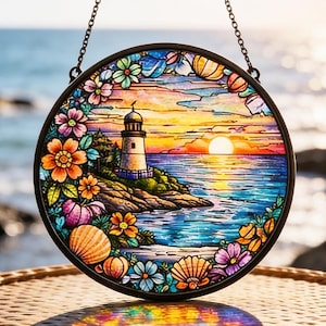 以下が含まれることがあります： 夕焼けの海岸に立つ灯台を描いた丸いステンドグラスパネル。カラフルな花と貝殻で縁取られ、吊り下げ用のチェーンが付いています。鮮やかな青、オレンジ、紫の色使いが特徴です。