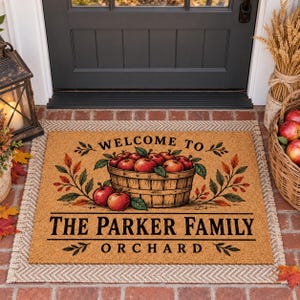 May include: A rectangular tan coir doormat featuring a printed illustration of a wooden basket filled with red apples. The text reads WELCOME TO THE PARKER FAMILY ORCHARD. The design includes decorative autumn leaves and branches.