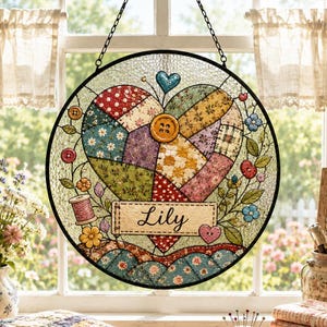 May include: A circular stained glass suncatcher featuring a central heart composed of various patterned fabric-like segments in red, blue, yellow, and green. A rectangular banner across the bottom displays the name Lily in black script lettering.