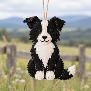 May include: A black and white felt dog ornament featuring a stitched border, a white chest patch, white paws, and a white tail tip, suspended by a thin brown string for hanging. The dog has a smiling expression with closed eyes.